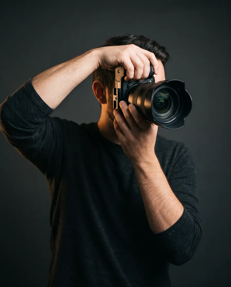 Photographe tenant son appareil devant le visage, sur fond sombre